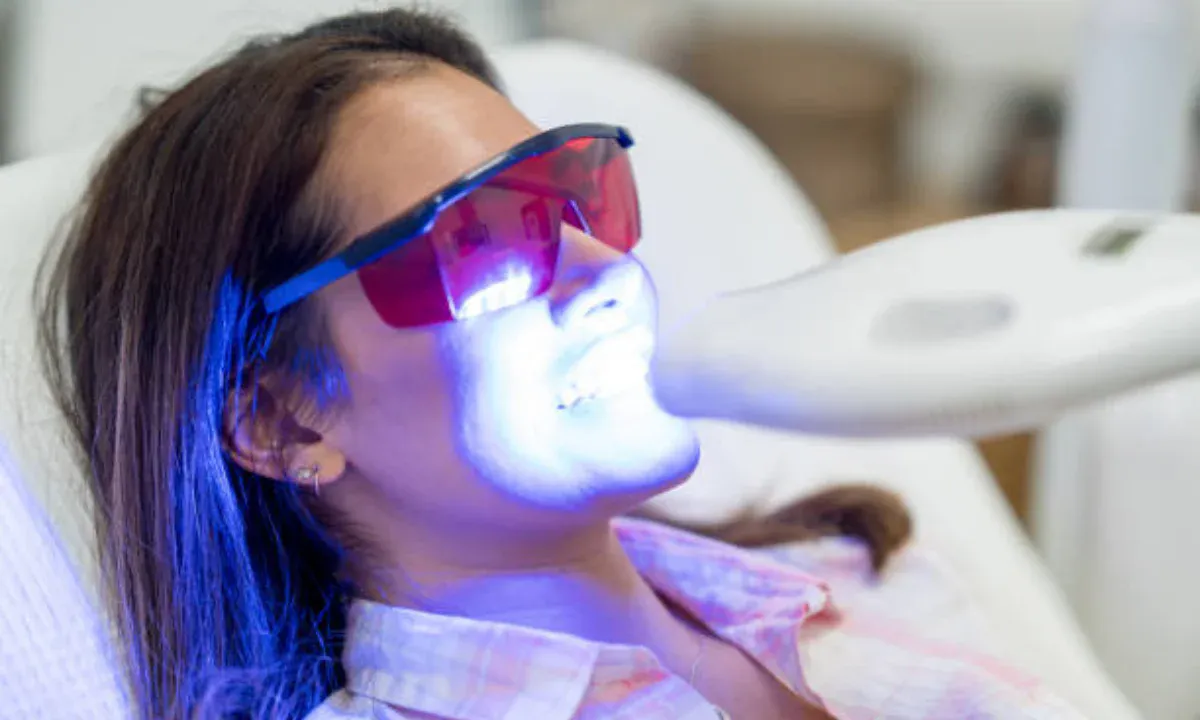 Woman receiving professional teeth whitening treatment with LED light and protective goggles